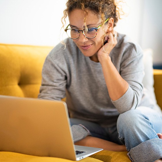 Woman with glasses smiling while looking at laptop