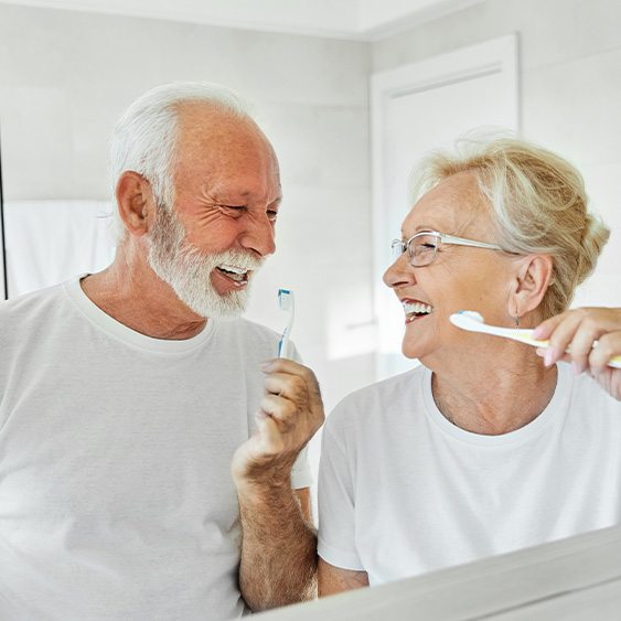 Senior couple smiling while brushing their teeth