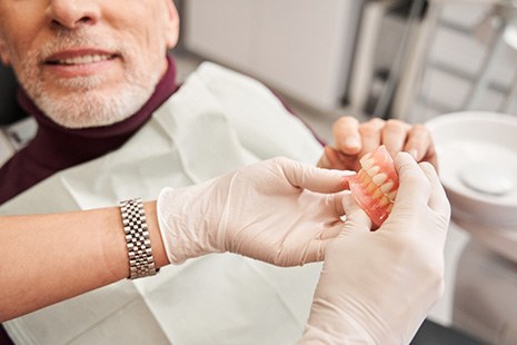 Gloved hands handing dentures to patient in dental chair
