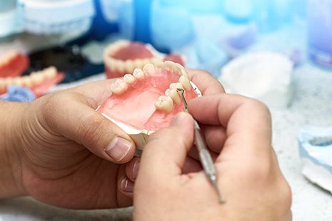 Hands refining the teeth on an arch of dentures