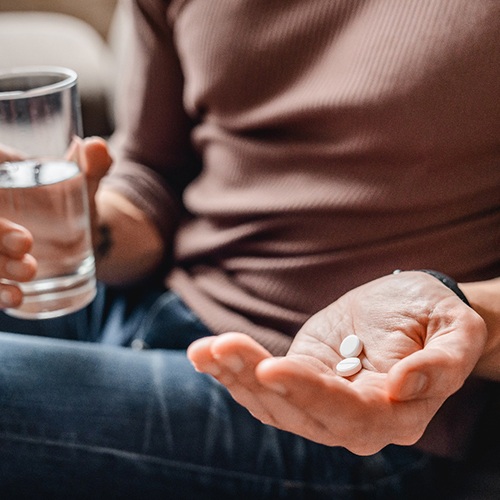 Chest-down view of person in brown shirt holding pills and glass of water