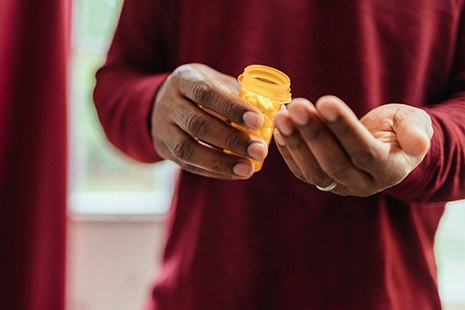Hands of man in red shirt pouring pills out of prescription bottle