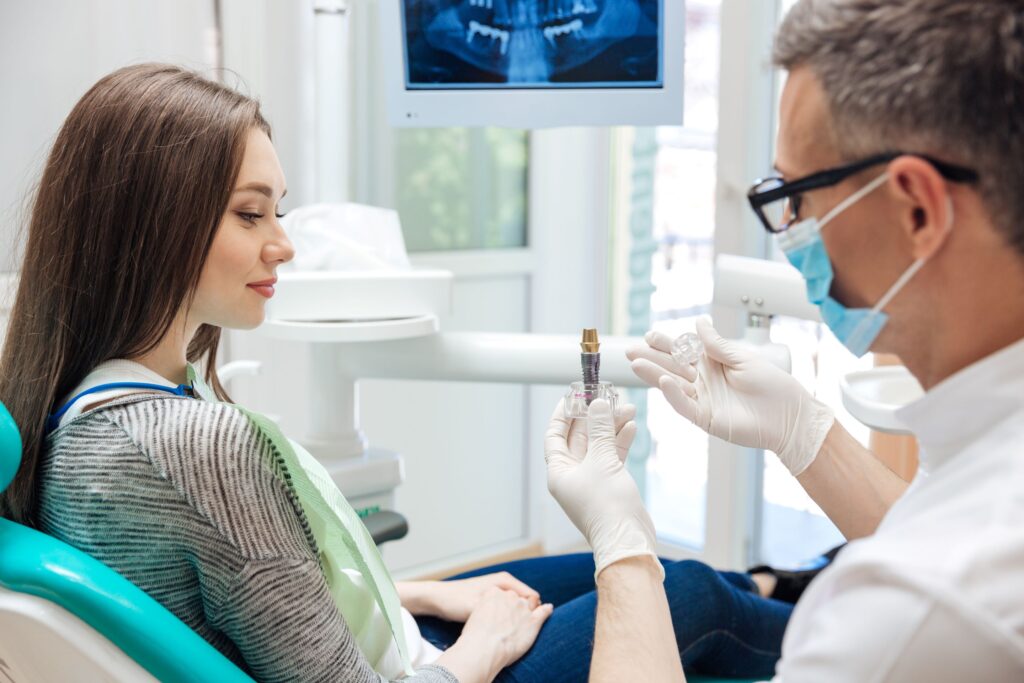 Dentist showing sample implant to woman in dental chair